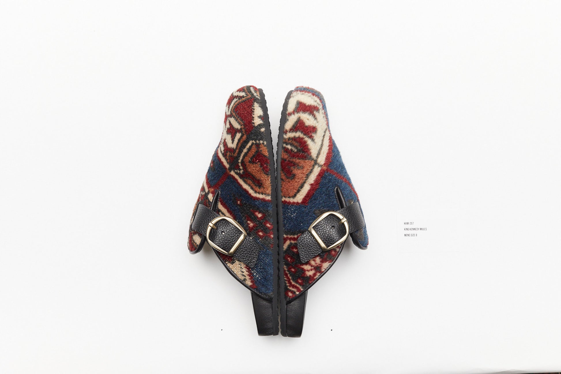 Buckle side view of rug mules.  King Kennedy Rug Mules are one-of-a-kind and made of 100 year old antique Persian rug fragments with soft lambskin footbed and rubber sole. This pair is made of an antique Persian rug with deep blue base and cream, red and tan medallion designs. 